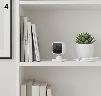 Blink Mini 2 small indoor security camera placed on a minimalist bookshelf.